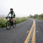 A person on a bicycle rides on a road in the fog